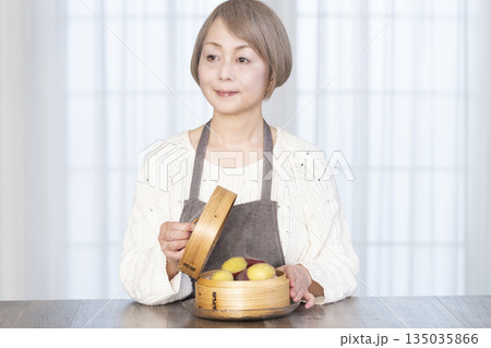 せいろでさつまいもを蒸して食べるシニア女性 135035866