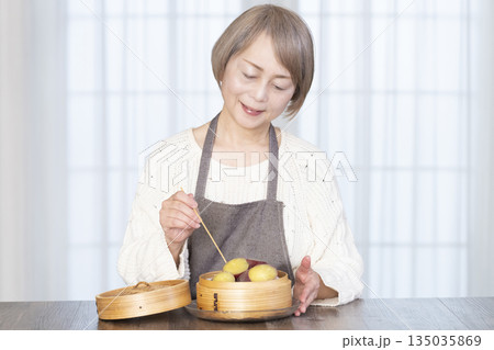 せいろでさつまいもを蒸して食べるシニア女性 135035869