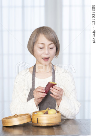 せいろでさつまいもを蒸して食べるシニア女性 135035889