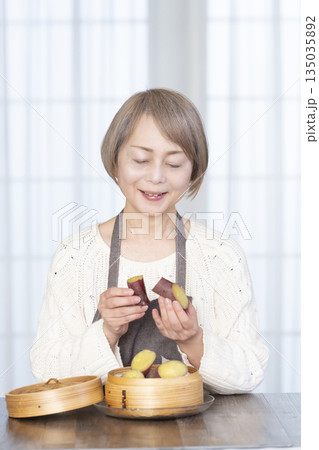 せいろでさつまいもを蒸して食べるシニア女性 135035892