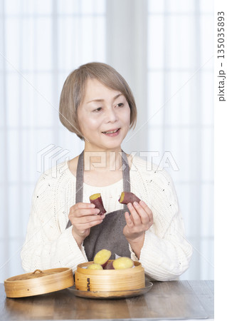 せいろでさつまいもを蒸して食べるシニア女性 135035893