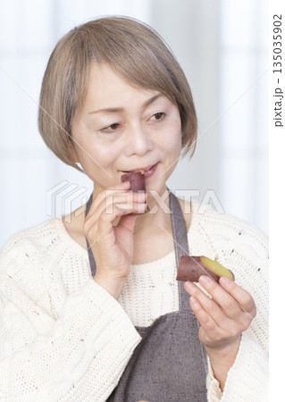 せいろでさつまいもを蒸して食べるシニア女性 135035902