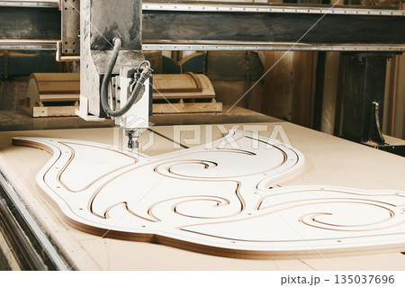 Numerically controlled woodworking machine cuts rounded complex lines on the canvas. Computer numerical control. CNC. Numerically controlled woodworking machine cuts rounded complex lines on the canvas. Computer numerical control. CNC. 135037696