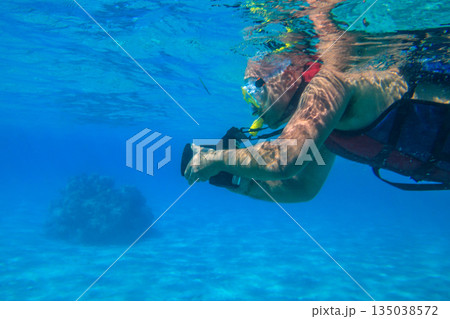 Man with photo camera taking photos and snorkeling underwater by coral reef in the Red sea, Egypt 135038572