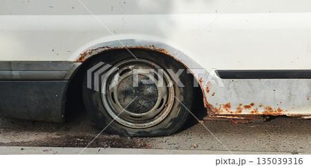 Rusted side of old white van with flat tire on urban street during day. Detail of corrosion and neglect on vehicle body panel and wheel arch. 135039316