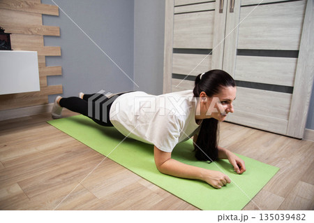 Woman performing plank exercise on yoga mat indoors. Fitness routine in apartment. Core strength workout. Healthy lifestyle activity for adults. 135039482