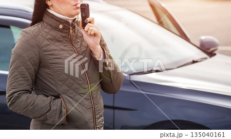 Responsible Female Driver Uses Breath Alcohol Tester. Standing By Her Vehicle Outdoors. Copy space for text 135040161