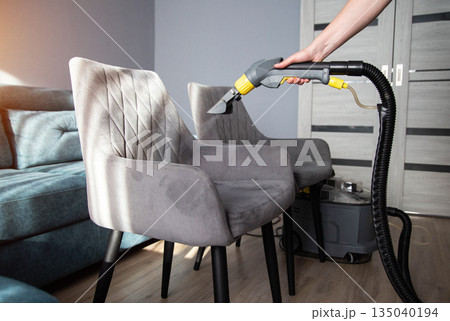 Cleaning plush chairs in a modern living room with a vacuum cleaner attachment Cleaning plush chairs in a modern living room with a vacuum cleaner attachment 135040194