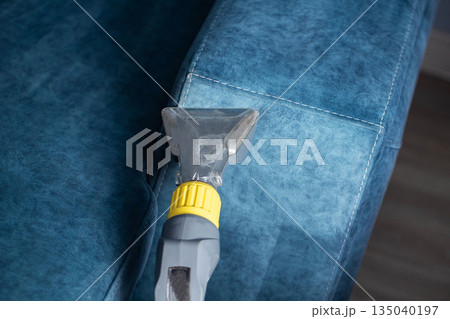 Cleaning a blue upholstered sofa with a steam cleaner in a modern living room setting during bright daytime 135040197