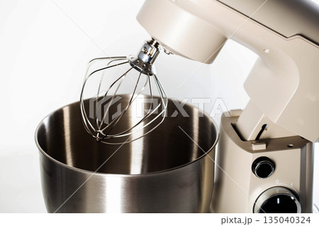 Close-up stand mixer with whisk attachment and stainless steel bowl against white background, kitchen appliance for baking and food preparation Close-up stand mixer with whisk attachment and stainless steel bowl against white background, kitchen appliance for baking and food preparation 135040324