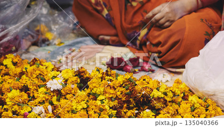 Woman making flower garland at night market in Delhi Woman making flower garland at night market in Delhi 135040366
