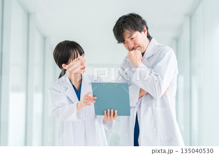 病院の通路でカルテを見ながら会話する白衣姿の男女の医師 135040530