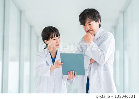 病院の通路でカルテを見ながら会話する白衣姿の男女の医師 135040531