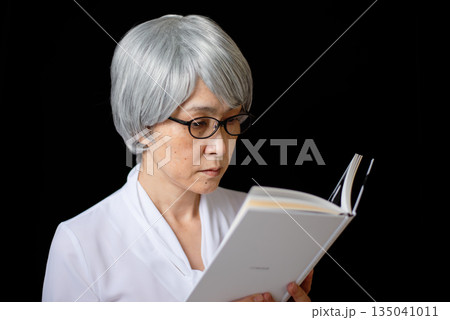 老眼鏡をかけて読書をする白髪のシニア女性 老眼鏡をかけて読書をする白髪のシニア女性 135041011