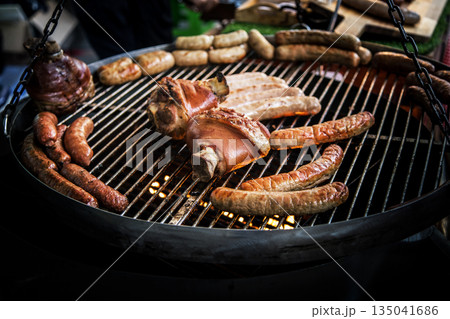 Smoked pork knuckle and grilled sausages on a barbecue grill, perfect for a hearty meal. Delicious, savory Smoked pork knuckle and grilled sausages on a barbecue grill, perfect for a hearty meal. Delicious, savory 135041686