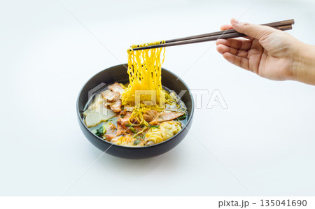 Hand picking yellow noodles from a pork noodle bowl on a white background for advertising 135041690