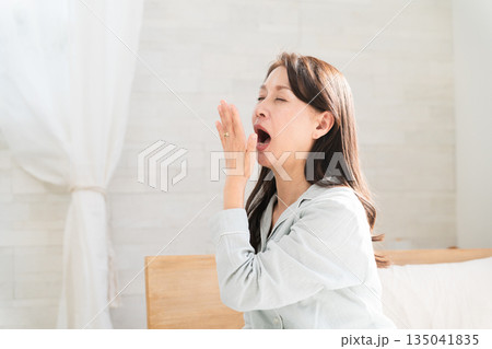 起きてベッドの上で伸びをする女性 135041835