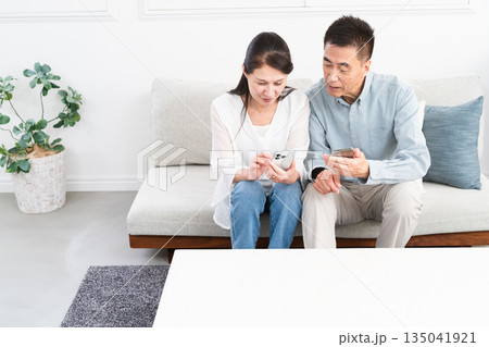 ソファーに座ってスマートフォンを操作している熟年夫婦　ライフスタイルイメージ 135041921