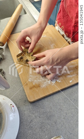 Hands cutting cookie dough with metal cutter on wooden board in home kitchen. This image represents homemade baking process creativity and traditional cooking 135041945