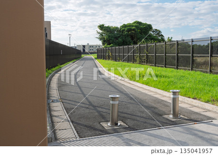 水道施設内の舗装された管理用道路と上下可動式の金属製車止めポール 135041957
