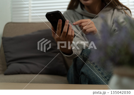 Cheerful woman use smartphone, enjoy personal chat exchanges messages through mobile application, learn new AI platform for business or fun, distracted from workflow on laptop in workplace. Cheerful woman use smartphone, enjoy personal chat exchanges messages through mobile application, learn new AI platform for business or fun, distracted from workflow on laptop in workplace. 135042030