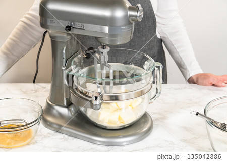Front view of an electric stand mixer in use, blending ingredients for Classic Sugar Cookie Dough. The baker hands are steadying the bowl as the mixer combines butter, sugar, and other ingredients on 135042886