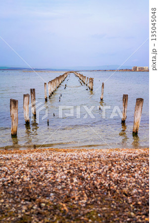 Old wooden pier remains stretch into shallow sea near Pomorie, Bulgaria, with soft blue sky Old wooden pier remains stretch into shallow sea near Pomorie, Bulgaria, with soft blue sky 135045048