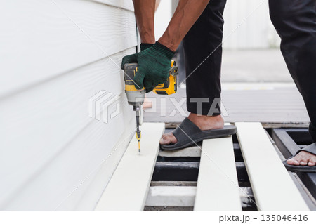 A worker is using a cordless power drill to fasten exterior floor boards. A worker is using a cordless power drill to fasten exterior floor boards. 135046416