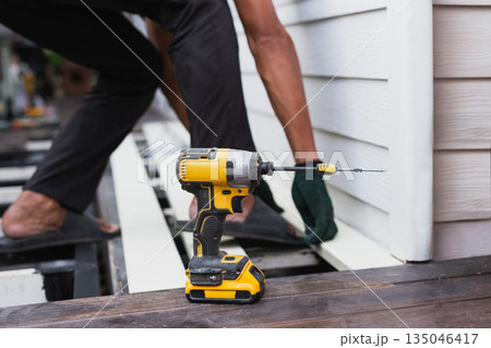 A construction worker is using a cordless power drill to install exterior siding on a house. 135046417