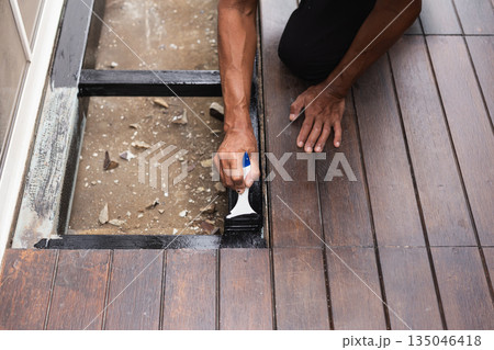 A professional painter is applying anti rust paint to a steel balcony outside a house. 135046418