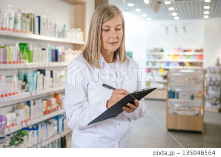 Female pharmacist making notes and looking involved Female pharmacist making notes and looking involved 135046564