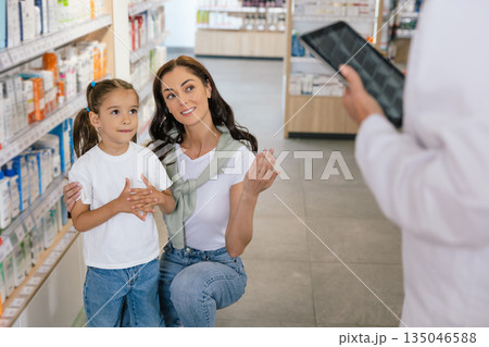 Pharmacist advising a young woman with a little girl on medicines 135046588