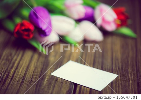 3D render showing blank white rectangular card on wooden tabletop featuring blurred tulip bouquet 3D render showing blank white rectangular card on wooden tabletop featuring blurred tulip bouquet 135047301