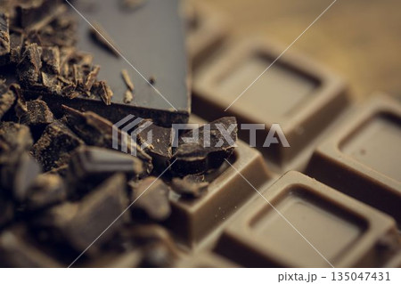 3D render is showing broken dark chocolate chunks resting atop milk chocolate bar with shallow blur 135047431
