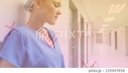 Holding tablet, nurse in blue scrubs reviewing records in ward corridor with overlays, copy space 135047656