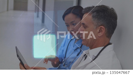 Reviewing tablet colleagues in scrubs and coats leaning against clinic hallway wall, copy space 135047667