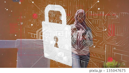Holding smartphone, woman with headscarf viewing screen in home office, laptop and padlock graphic Holding smartphone, woman with headscarf viewing screen in home office, laptop and padlock graphic 135047675