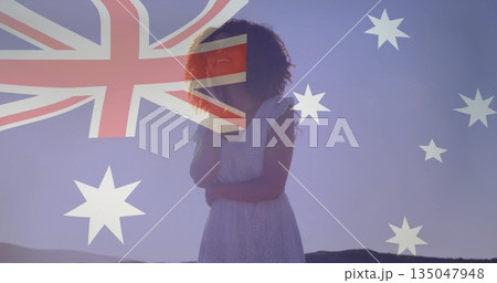Standing woman wearing white lace dress on dawn hills, with translucent Australian flag overlay Standing woman wearing white lace dress on dawn hills, with translucent Australian flag overlay 135047948