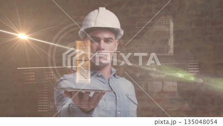 Holding tablet, denim-clad engineer wearing white helmet projecting 3D model in office, with data 135048054