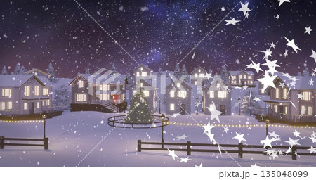 Glowing Christmas tree standing in village plaza at night with railing, string lights and lampposts 135048099