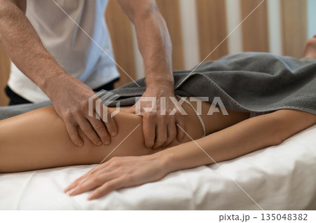 Masseur doing legs massage to a woman lying on a couch Masseur doing legs massage to a woman lying on a couch 135048382