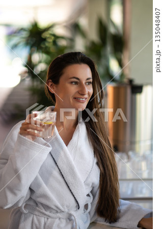 Woman in white bathrobe drinking hot water with lemon Woman in white bathrobe drinking hot water with lemon 135048407