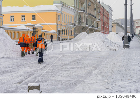 City workers in reflective uniforms clear massive snow piles from urban street after snow storm. Winter urban infrastructure, climate adaptation, urban maintenance City workers in reflective uniforms clear massive snow piles from urban street after snow storm. Winter urban infrastructure, climate adaptation, urban maintenance 135049490