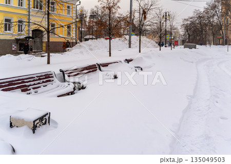 After snowstorm in city. Snow covered benches in city park almost fully buried after record snowfall near residential area. Concept of climate change, failed maintenance, urban winter paralysis 135049503