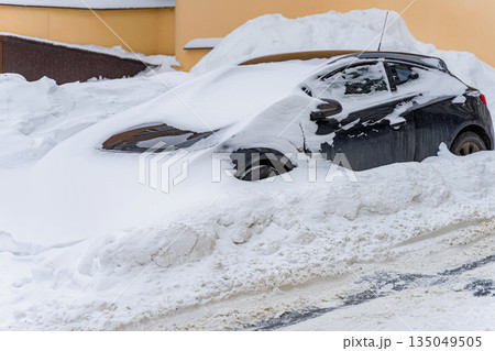 Winter problem, snow in city. Black car stuck in deep snow near residential building after snowstorm. Concept of winter difficulties, road blockage, frozen transportation, snowfall aftermath 135049505