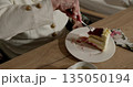 Older woman savoring delicious layered cake. Close-up shot of hand holding fork. Creamy dessert with berry topping on plate. Cozy and relaxed atmosphere. 135050194