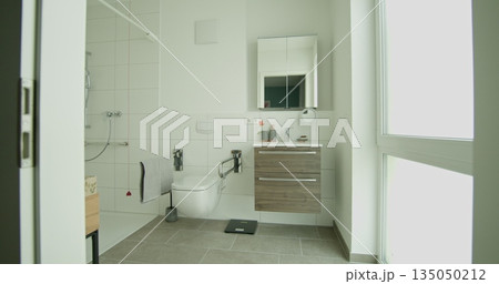 Contemporary bathroom with wheelchair accessible shower and modern vanity. White tiles and natural light create clean and bright space. Design includes accessible features for ease of use. 135050212