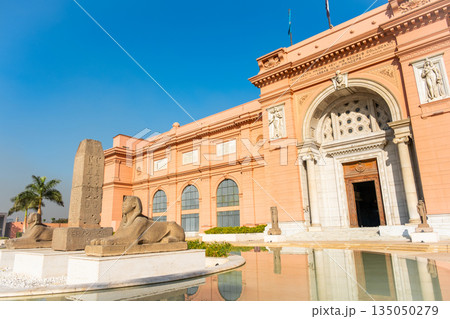 Cairo Museum at Tahrir Square features a grand facade with large windows and intricate architectural details. A stone sphinx sculpture is visible in the foreground Cairo Museum at Tahrir Square features a grand facade with large windows and intricate architectural details. A stone sphinx sculpture is visible in the foreground 135050279