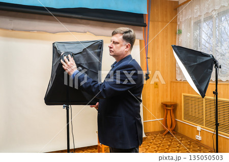 Photographer turning on softbox lighting equipment in a professional photo studio setup for portrait or product photography Photographer turning on softbox lighting equipment in a professional photo studio setup for portrait or product photography 135050503