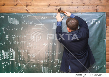 Photographer hammering a themed backdrop onto the wall for a school-themed photo session in a studio Photographer hammering a themed backdrop onto the wall for a school-themed photo session in a studio 135050508